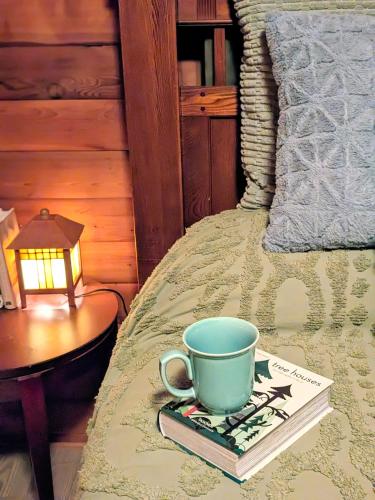 a bed with a cup and a book and a lamp at Cozy Copper Cabin Lodge in Sioux Falls