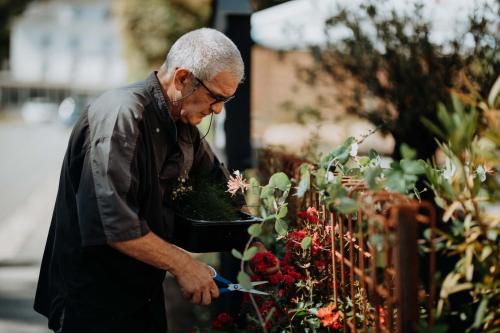 an older man cutting a plant in a garden at Hotel Restaurant Le Cigalon in Waldbillig