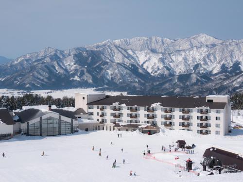 a large building in the snow with mountains in the background at Hotel Harvest Skijam Katsuyama in Katsuyama