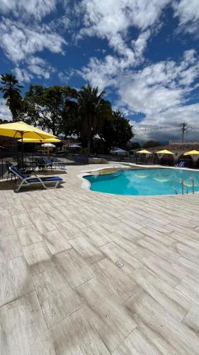 a swimming pool with a yellow umbrella and chairs and tables at Hotel El Castillo Chinauta in Chinauta