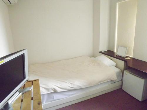 a small bedroom with a bed and a television at Rakuda Hotel Jingu in Miyazaki