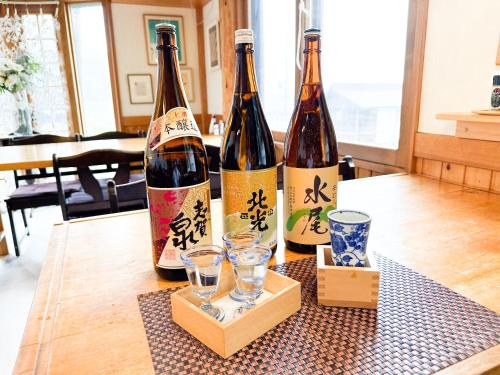 three bottles of wine sitting on a table with glasses at Koguma no ie in Nozawa Onsen