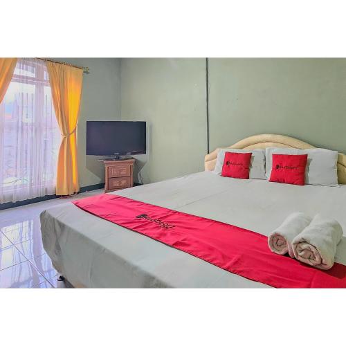 a bedroom with a large bed with red pillows and a television at RedDoorz at Linggarjati Kuningan in Kuningan