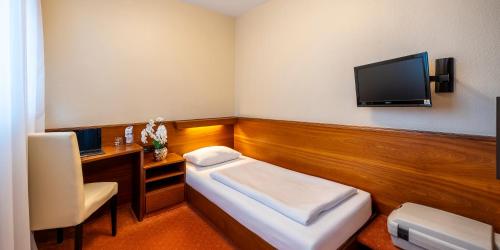 a room with a bed and a desk and a tv at PLAZA INN Rieker Stuttgart Hauptbahnhof in Stuttgart
