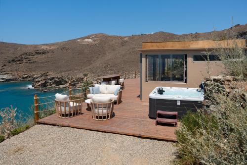 a deck with a hot tub and chairs and a house at Blueros Luxury Villa in Megas Yialos-Nites
