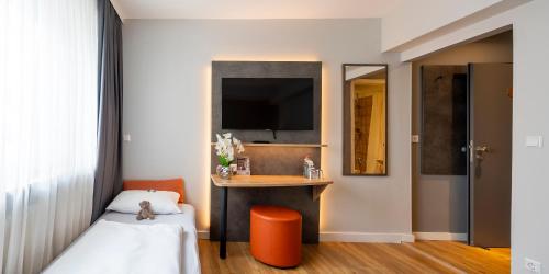 a bedroom with a bed and a desk with a tv at PLAZA INN Rieker Stuttgart Hauptbahnhof in Stuttgart