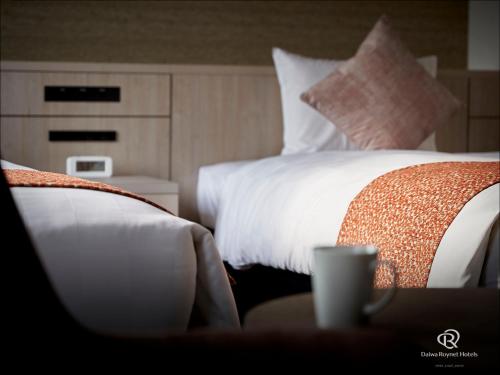 a hotel room with two beds and a cup on a table at Daiwa Roynet Hotel Kyoto-Hachijoguchi in Kyoto
