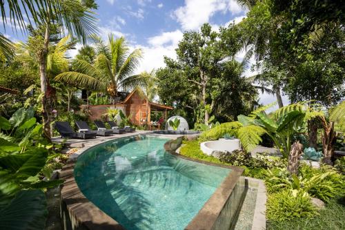 a swimming pool in a garden with chairs and trees at Berlima Wooden Lodge by GenuineHost in Ubud
