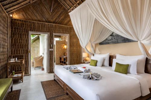 a bedroom with a large white bed with curtains at The Mesare Eco Resort in Nusa Penida