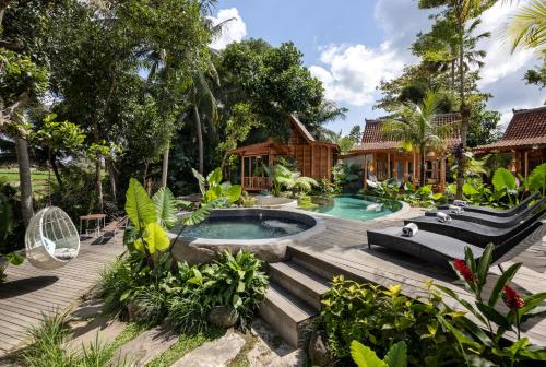 a tropical garden with a pool and a house at Berlima Wooden Lodge by GenuineHost in Ubud