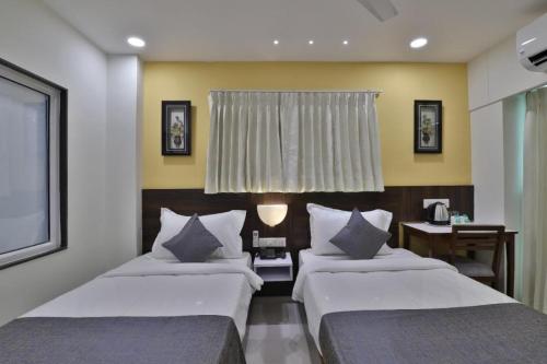 a bedroom with two beds and a table and a window at Leo Hotel in Ahmedabad