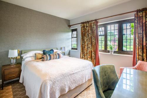 a bedroom with a bed and a chair and windows at Mallory Court Country House Hotel & Spa in Leamington Spa