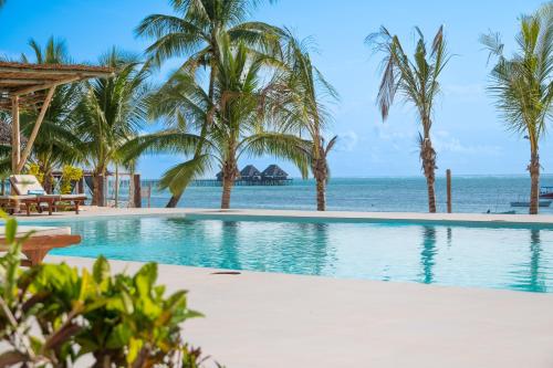 a swimming pool with palm trees and the ocean at Ocean Boutique Hotel - Adults only in Pingwe