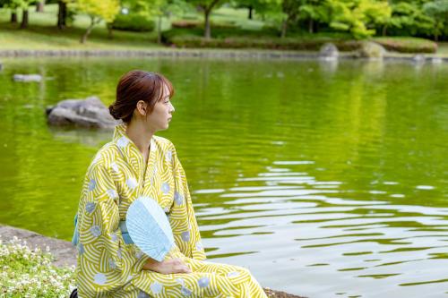 a woman in a kimono sitting next to a pond at Ichiraku tendo spa & brewery in Tendo