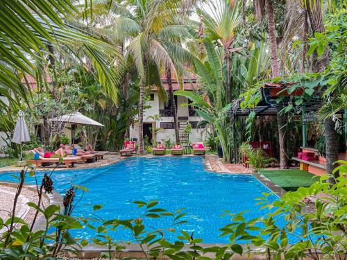 a swimming pool with palm trees and people sitting around it at Natural Relax Villa in Siem Reap