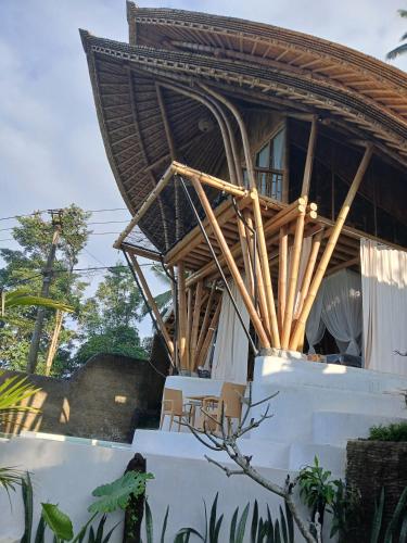 a building with a straw roof with a table and chairs at Danaswari Bali Bamboo House in Selat
