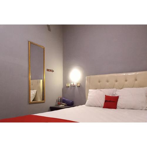 a bedroom with a bed with a red pillow and a mirror at RedDoorz at Deluxe Hotel near Terminal Purabaya Bungurasih in Sidoarjo