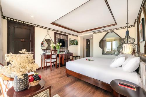 a bedroom with a large bed and a desk at Qualia De Hôtel Hoi An - Rooftop Bar City View in Hoi An