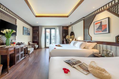 a hotel room with two beds and a desk at Qualia De Hôtel Hoi An - Rooftop Bar City View in Hoi An