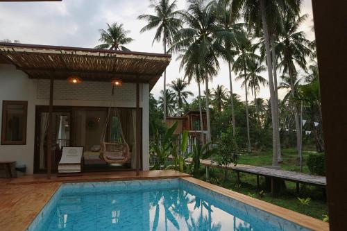 a swimming pool in front of a house with palm trees at บ้านพราวพร้าว Baan Proud Proud in Khanom