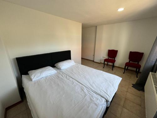 a bedroom with a white bed and two red chairs at HIDO Landhaus am See in Xanten