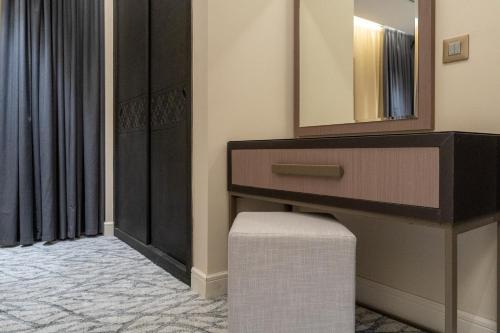 a bathroom with a vanity with a mirror and a stool at The Address Serviced Apartments in Al Khobar