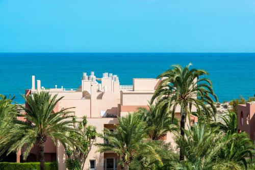a building with palm trees in front of the ocean at Oliva Nova Beach & Golf Hotel in Oliva