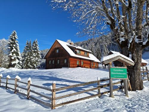 a log cabin in the snow with a fence and a sign at Ferienhaus Hinterhabneralm in Petersberg