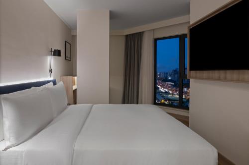 a white bed in a hotel room with a large window at Hampton By Hilton Istanbul Merter in Istanbul