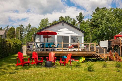 a house with a deck with chairs and an umbrella at La Cozy O-Lac Magog in Sherbrooke