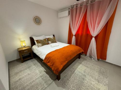 a bedroom with a bed with an orange blanket and a window at Magnifique T3 in Cayenne