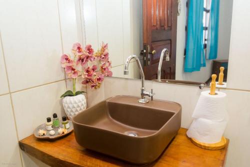 ein Waschbecken im Bad mit einem Spiegel und Blumen in der Unterkunft Casa Vila do Sol - 4 suítes - Praia da Taíba in Taíba