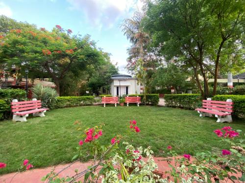 two park benches in a yard with pink flowers at Button Eyes Resort - Pet friendly in Hyderabad