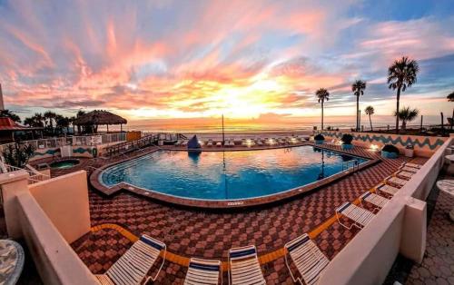 a pool with chairs and a sunset in the background at Luxury Beach Condo with Pool and Tiki Bar! in Daytona Beach
