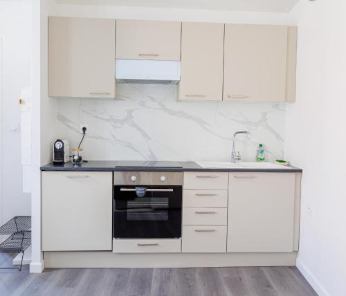 une cuisine avec des armoires blanches et un four noir dans l'établissement Le Cocon Cormeillais, à Cormeilles-en-Parisis