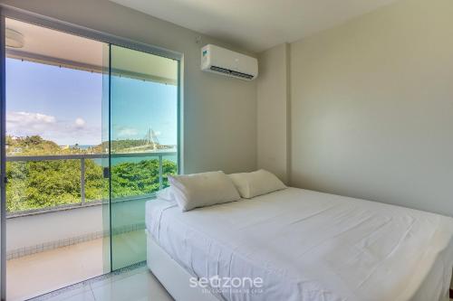 a bedroom with a white bed and a large window at Apto vista p/ rio c/ varanda - Pontal BCL402 in Ilhéus