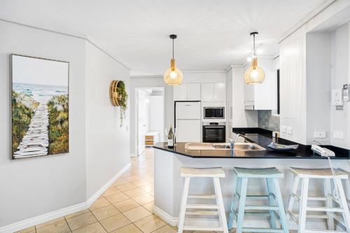 a kitchen with white cabinets and blue bar stools at By The Beach - Clubb Coolum Beachside Resort in Coolum Beach