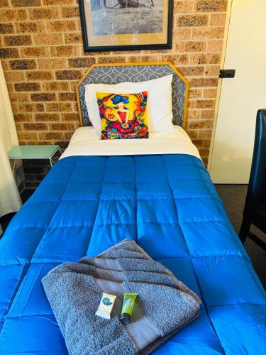a bed with a blue comforter and a pillow at Town and Country Motor Inn in Tamworth