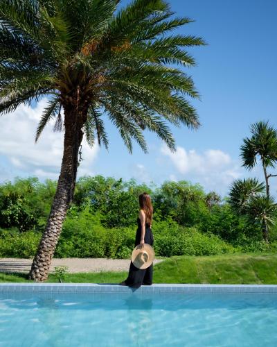 a woman in a black dress standing next to a palm tree at アヤンナ宮古島 in Miyako Island