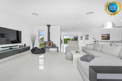 a white living room with a couch and a fireplace at Sea La Vie - Pet Friendly with Fireplace and Swimming Pool & Spa in Culburra Beach