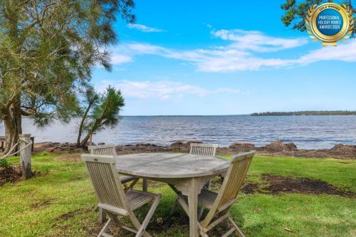 a table and chairs sitting next to the water at The Waterfront House - Pet Friendly - Absolute Waterfront in Erowal Bay