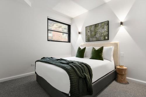 a white bedroom with a bed with green pillows at The Henrietta Apartments by Urban Rest in Sydney