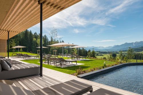 an outdoor deck with a pool and tables and umbrellas at PANORAMA Allgäu Spa Resort in Seeg