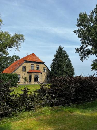 an old house with an orange roof on a field at Meekhofsveen in Appelscha