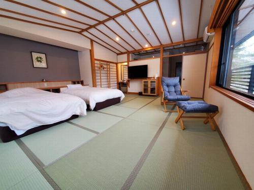 a bedroom with two beds and a chair and a television at 蔵王温泉 岩清水料理の宿 季の里 in Zao Onsen