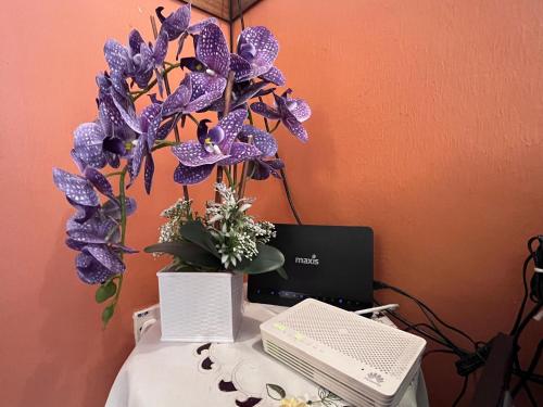 a vase of purple flowers on a desk with a laptop at Rumah Tamu by Perdana Hōmes for Múslim only in Sungai Petani