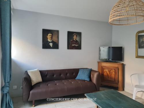 d'un salon avec un canapé marron et des photos murales. dans l'établissement Logis Philiberte 3 chambres centre bourg des Epesses à 5min du Puy du Fou, aux Épesses