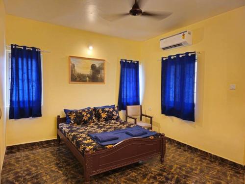 a bedroom with a bed with blue curtains and a fan at Casa de Bella in Candolim