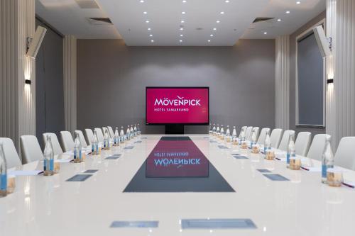 a conference room with a long table with chairs and a screen at Mövenpick Samarkand in Samarkand
