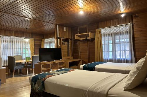 a room with two beds and a desk with a television at Hotel Pesona Bamboe Lembang in Genteng